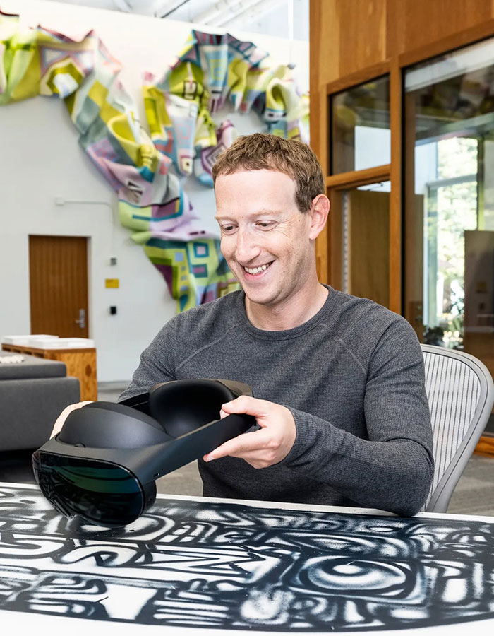 Mark Zuckerberg smiling while holding a VR headset indoors, related to embarrassing hot mic moment with Donald Trump.