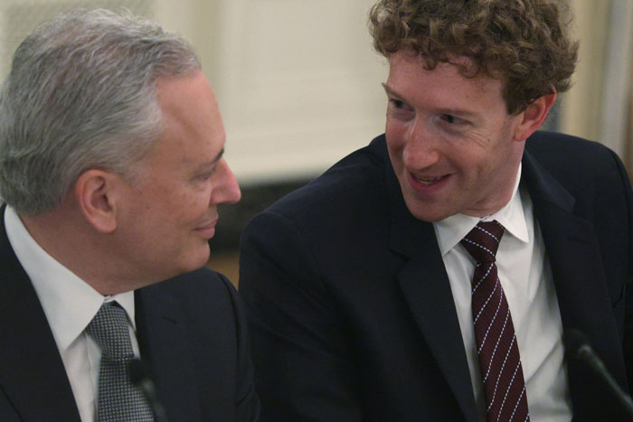 Mark Zuckerberg and a man in suits sharing a moment during a meeting, highlighting a hot mic incident with Donald Trump.