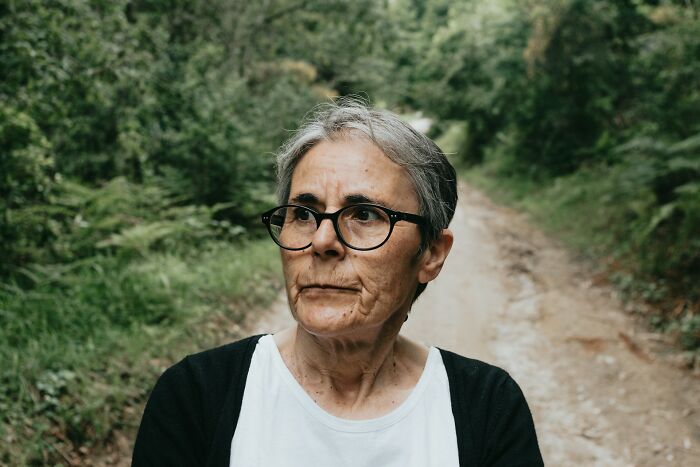 Older woman with glasses standing on a forest path, illustrating adults who failed to understand growing up is mandatory.