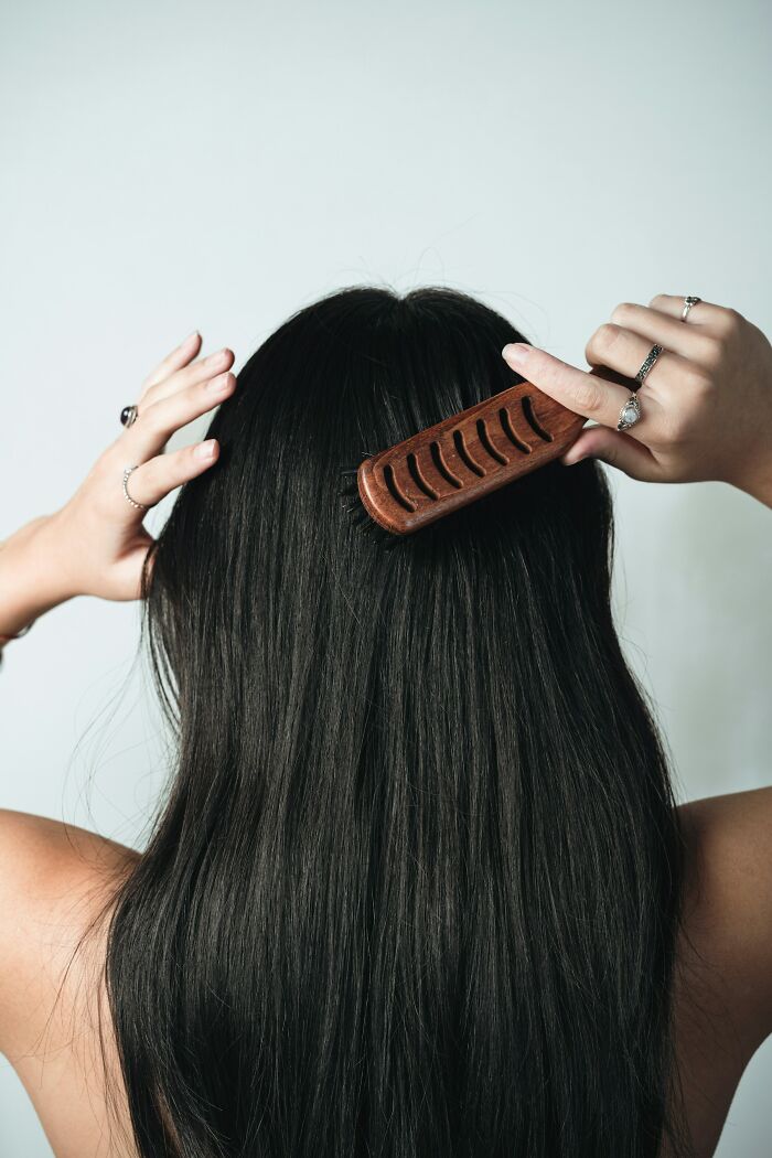 Person with long black hair combing with wooden brush, illustrating everyday things that humble fully grown adults.