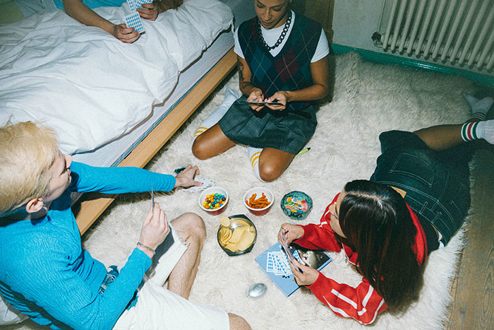 Group of young adults playing cards on floor with snacks, illustrating awkward social moments involving boxers bothering guests.