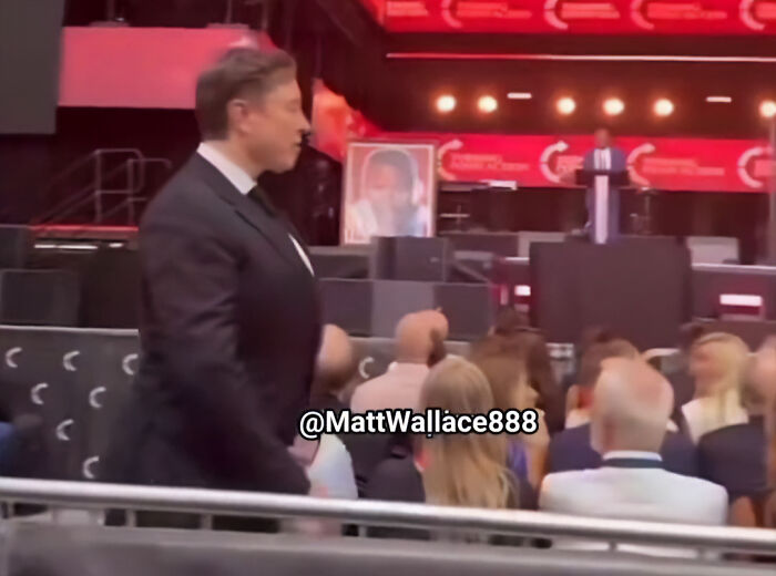 Elon Musk walking in a suit at an event, sparking wild conspiracy theories after a weird move at Charlie Kirk funeral.