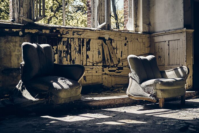 Two old, worn armchairs in a decayed room with peeling paint, evoking eerie underground exploration stories.
