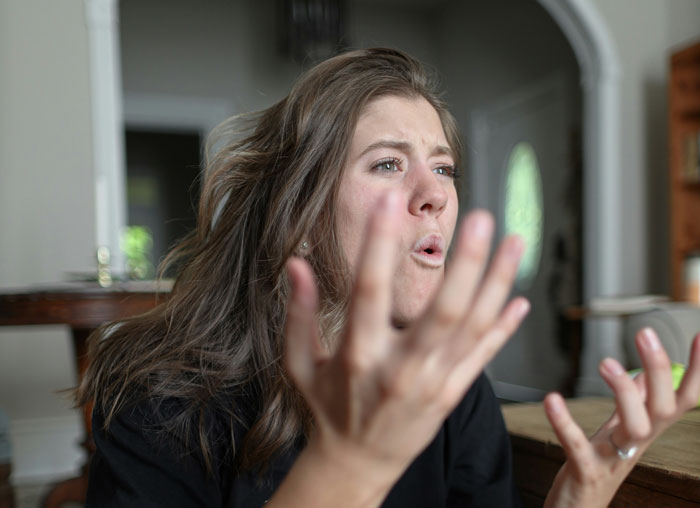 Woman with long hair gesturing angrily in a home setting during a confrontation linked to a school project at a wedding