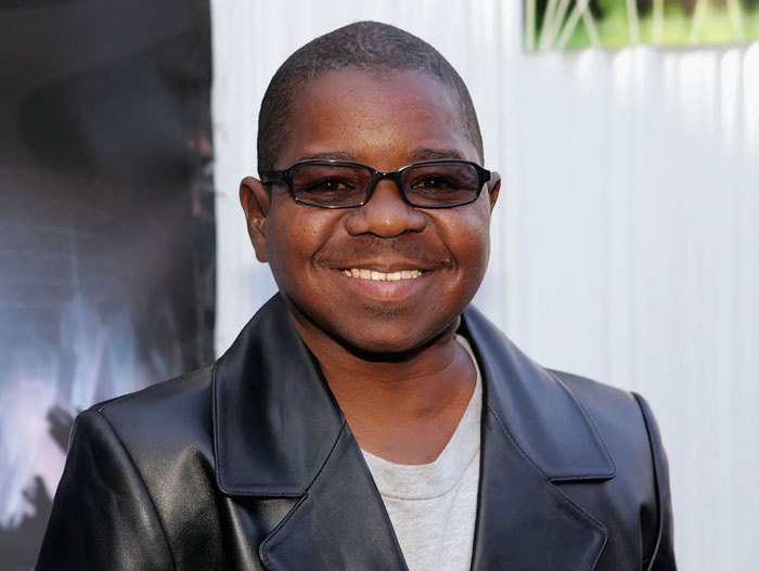 Smiling young male child star wearing glasses and a black leather jacket at an outdoor event for child stars who passed away.