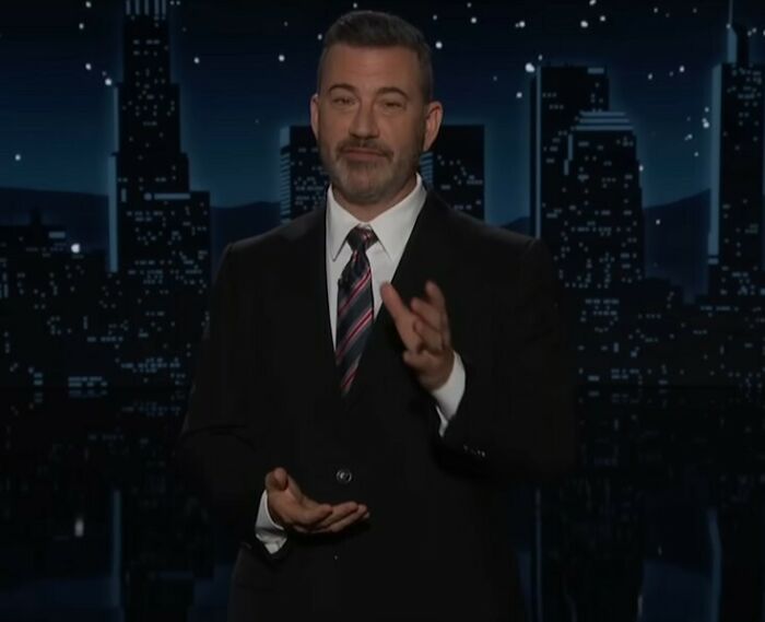Jimmy Kimmel standing on stage in a suit with city skyline background, addressing staff mutiny concerns. Jimmy Kimmel standing on stage in a suit with city skyline background, addressing staff mutiny concerns.
