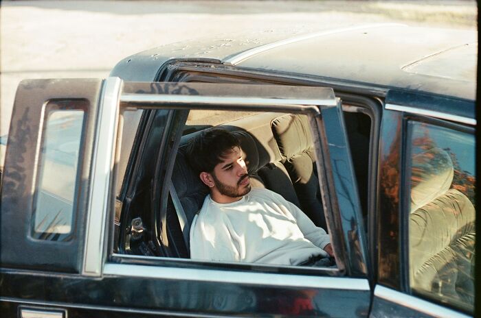 Young man sitting in a car looking contemplative, illustrating the impact of drained savings in one go stories.