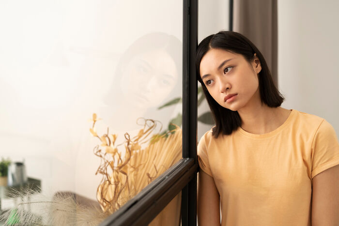Young woman in a yellow shirt reflecting sadly by a window, illustrating life after high school sports glory days.