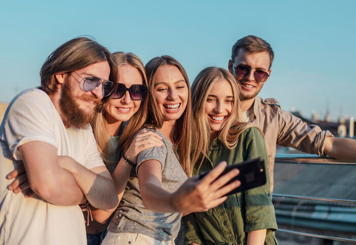 Group of young adults smiling and taking a selfie outdoors, representing people whose glory days were in high school.