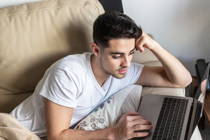 Young man lying on couch looking thoughtfully at laptop, reflecting the reality of former high school stars after glory days.