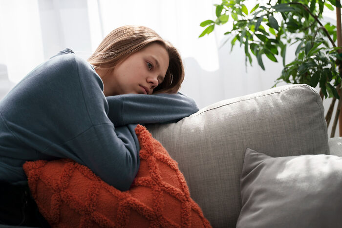 Teen woman reflecting on life’s changes after high school, resting on a couch with a thoughtful expression.