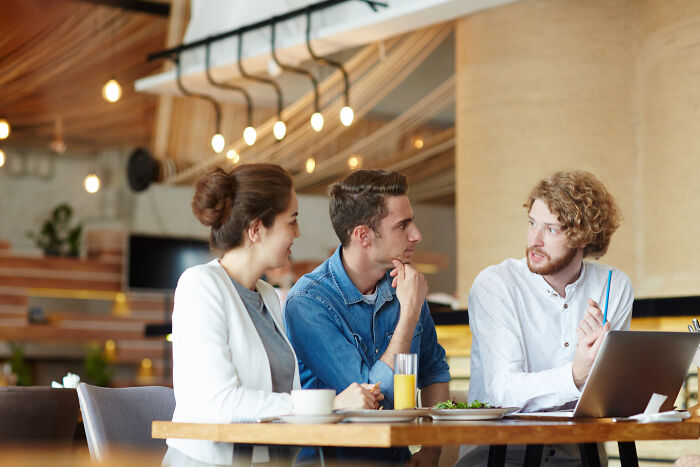 Three young adults discussing life after high school, sharing stories and plans in a modern café setting.