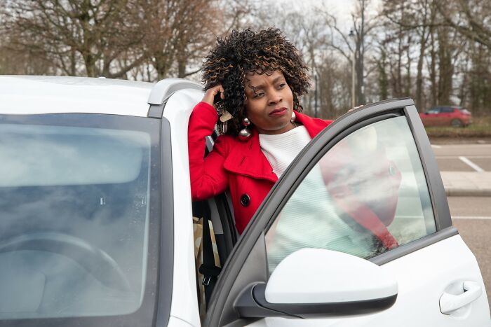 Woman in red coat standing by car door looking frustrated, representing dumbest and out of touch things told to people.