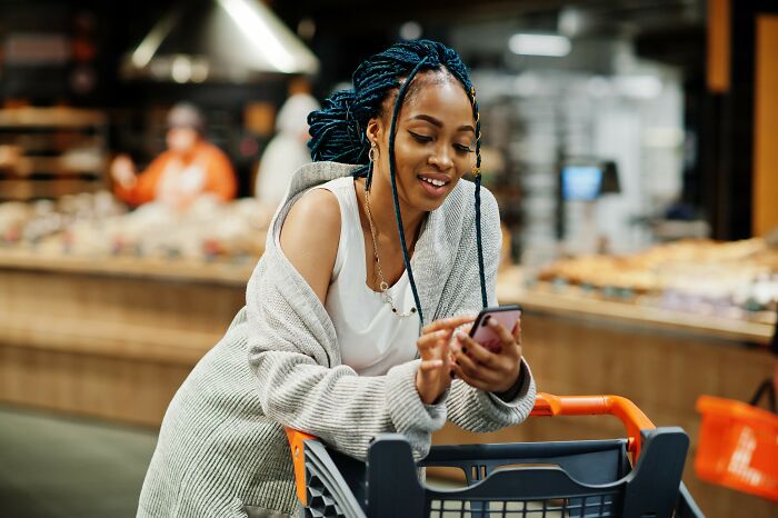 Young woman shopping in a store using her phone, exemplifying Americans finding a loophole and using it.