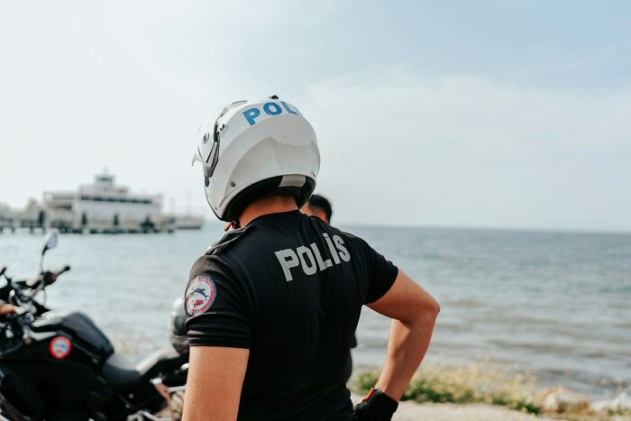 Police officer in helmet standing by motorcycles near water, representing innocent people blamed by police cases.
