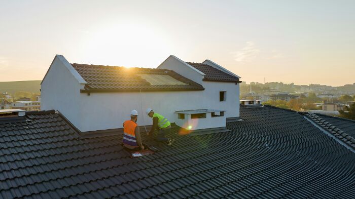 Two workers in safety vests repairing a rooftop at sunset, symbolizing how a single event can cause loss of savings.