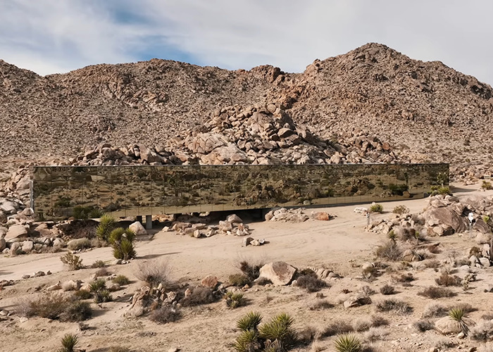 Mirrored invisible house blending into desert landscape with rocky hills, noted for Airbnb owners charging influencer fee.