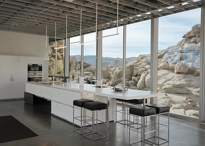 Modern kitchen interior with large windows showcasing rocky landscape at invisible house Airbnb owners charge influencer fee
