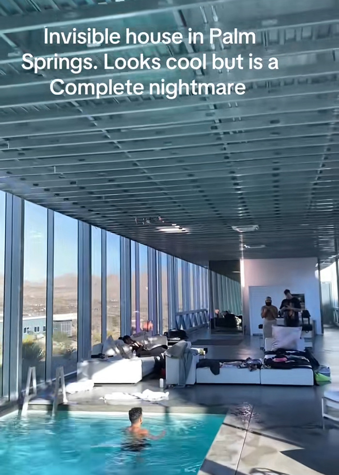 Interior view of the famous invisible house Airbnb with large glass walls and a person swimming in the pool inside.