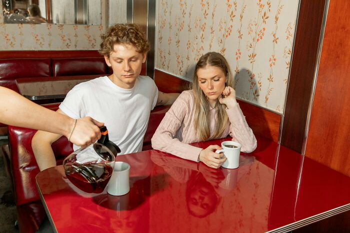Young couple at a diner, looking disappointed and awkward, capturing moments of dating an idiot experiences.
