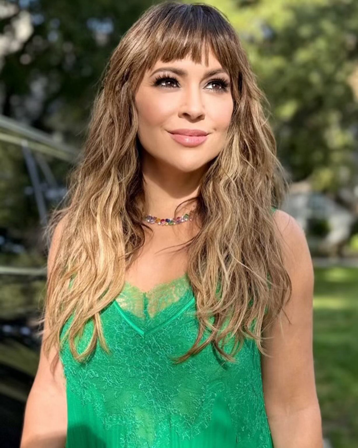 Alyssa Milano outdoors wearing a green lace top, smiling softly with long wavy hair in natural sunlight discussing breast implants.