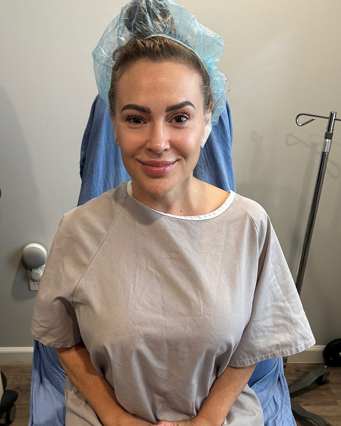 Alyssa Milano sitting in medical gown and surgical cap before breast implant removal procedure.