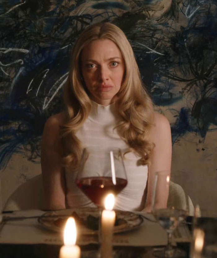 Amanda Seyfried sitting at a candlelit dinner table with wine glass, reacting seriously in a dimly lit setting. Amanda Seyfried sitting at a candlelit dinner table with wine glass, reacting seriously in a dimly lit setting.