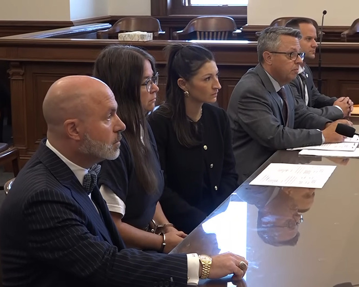 Amish mom sitting with lawyers in courtroom during a hearing about drowning 4-year-old son case.