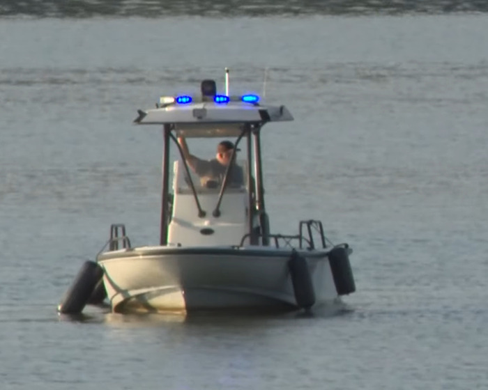 Police officer on a boat with blue lights patrolling calm water after Amish mom's chilling confession goes viral