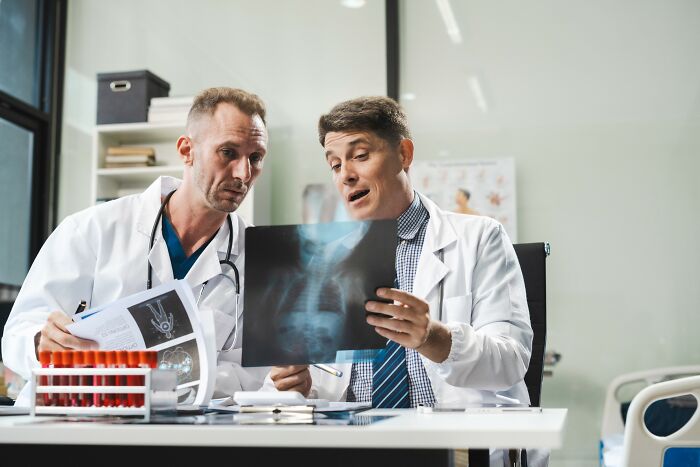 Two doctors examining an X-ray and medical documents, discussing unusual patient cases that defied medical odds.
