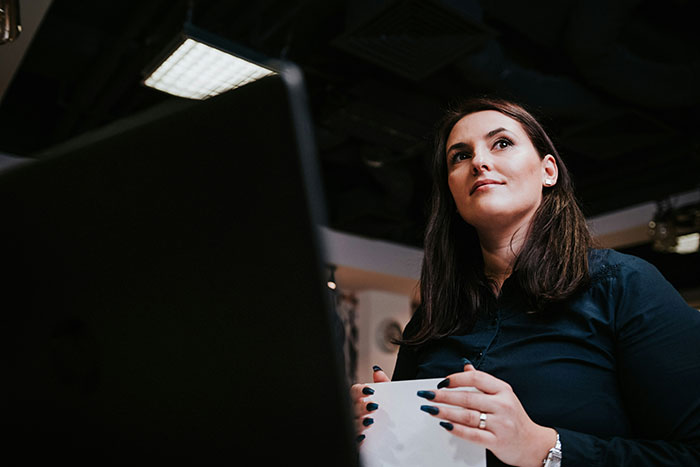 Woman at office desk with dark hair and navy shirt, holding paper, showing a petty response to creepy coworker.