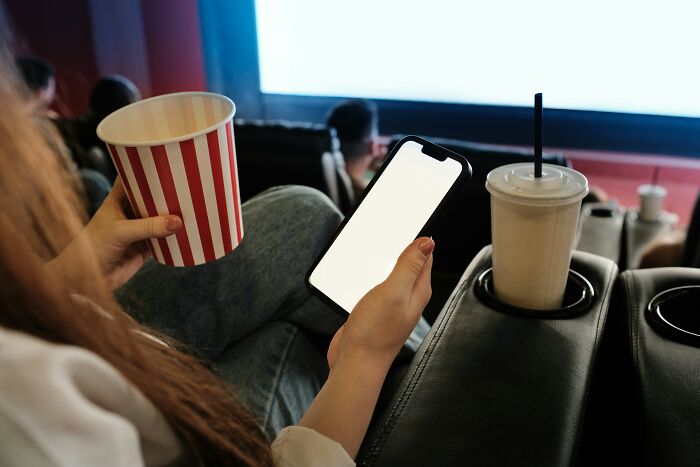 Person holding a phone and popcorn in a theater, with people sharing sounds in an extremely angry setting.