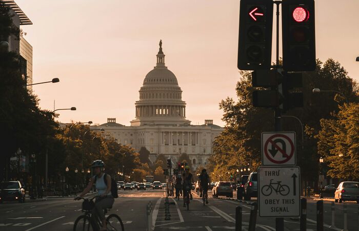 Cyclists ride along a busy city street at sunset with the Capitol building in the background, showing everyday things.