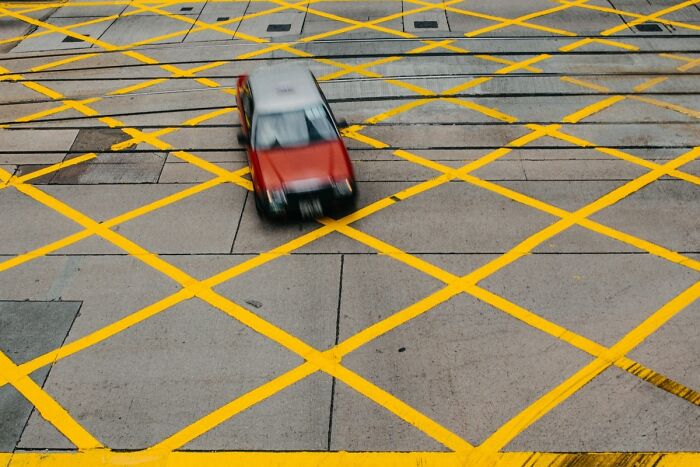Red and gray car navigating a marked yellow grid on concrete, illustrating Americans finding a loophole in traffic rules.