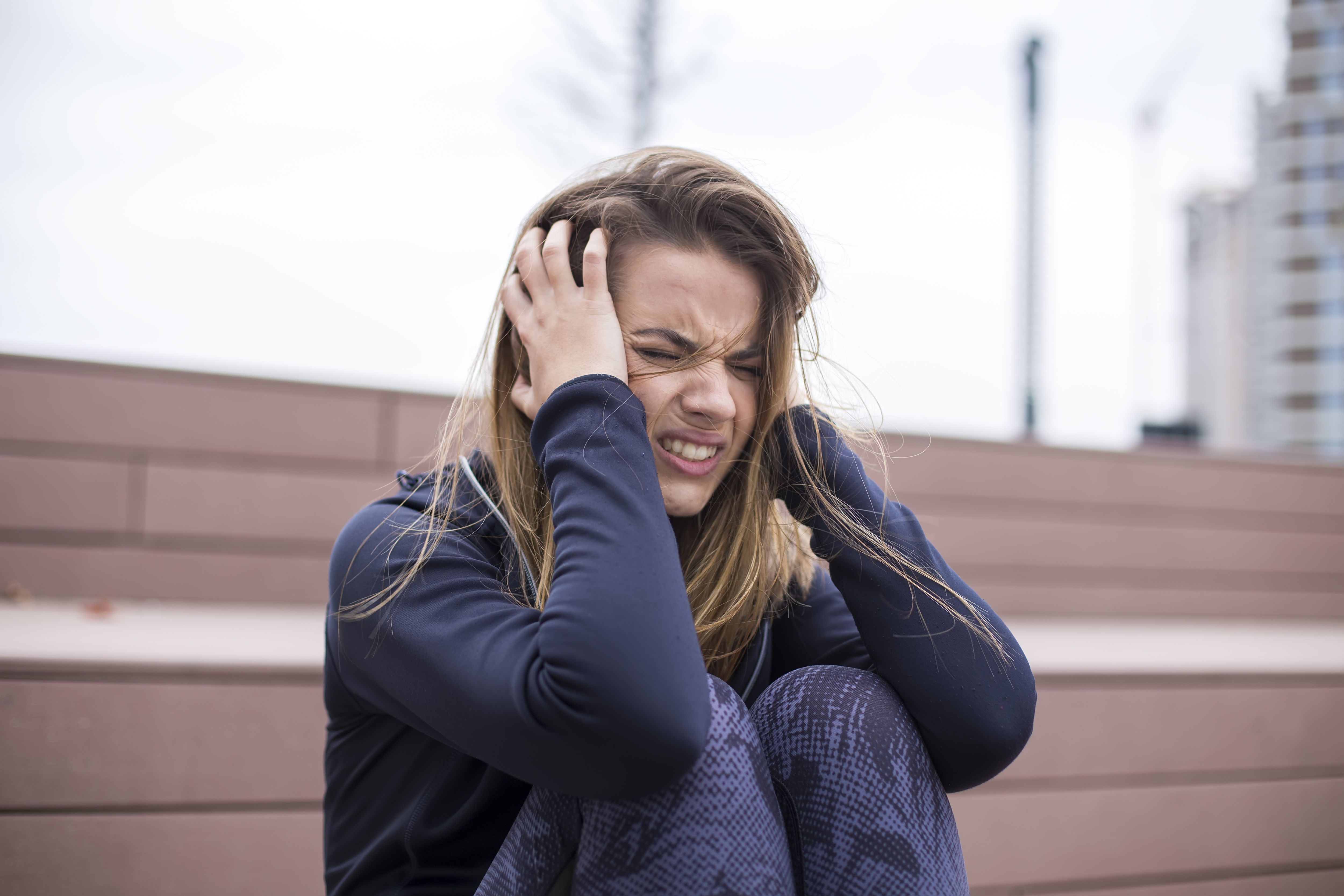Young woman crying and distressed outdoors, expressing emotion related to demands and refusal in a backyard setting.