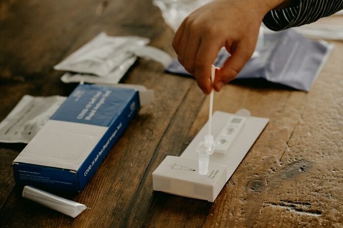 Person using a Covid test kit on wooden table, relating to groom insisting guest can attend wedding despite positive test.