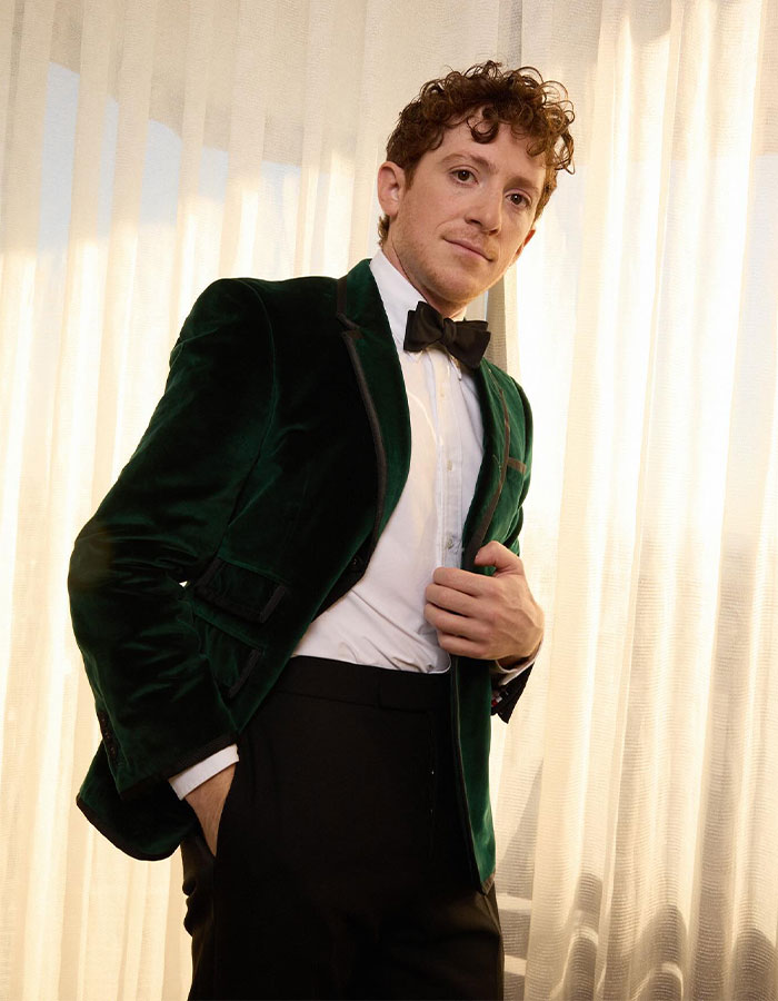 Ethan Slater wearing a green velvet tuxedo jacket and bow tie, posing indoors amid breakup rumors with Ariana Grande. Ethan Slater wearing a green velvet tuxedo jacket and bow tie, posing indoors amid breakup rumors with Ariana Grande.
