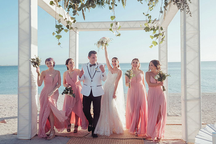 Bride smiling with groom and bridesmaids in pink dresses at a beach wedding, woman remarried but upset about cheater ex. Bride smiling with groom and bridesmaids in pink dresses at a beach wedding, woman remarried but upset about cheater ex.