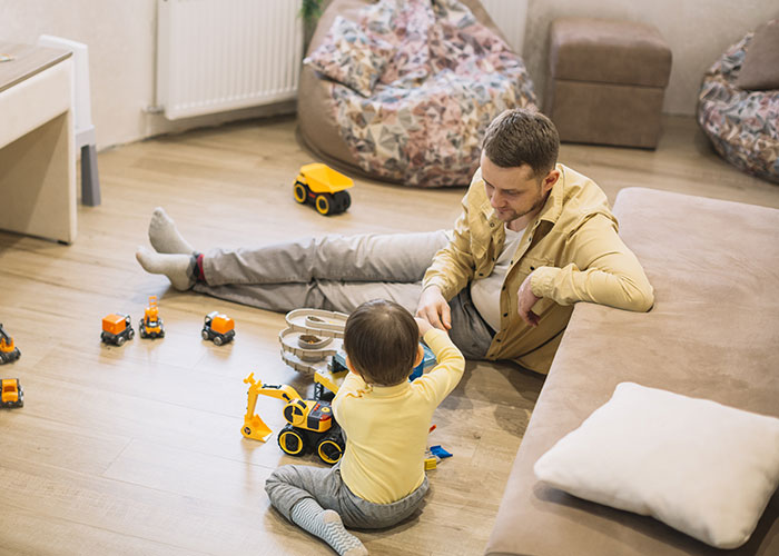 Father watching kids and playing with toy trucks in living room while wife cooks nearby in a cozy home setting. Father watching kids and playing with toy trucks in living room while wife cooks nearby in a cozy home setting.