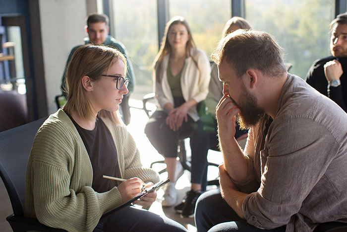 A group discussing a siblings loss and HOA conflict while seated indoors in a serious conversation.