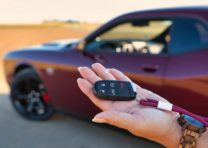 Person holding car keys in front of a parked red car, illustrating wildest rules people grew up with.