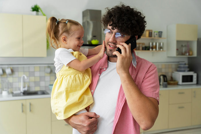 Dad holding little girl in kitchen while talking on phone, concerned about eating disorder comments and child's food aversion.