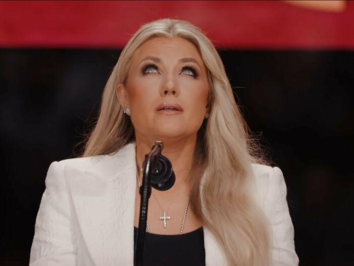 Erika Kirk wearing a white jacket and cross necklace, looking up during a public moment amid viral internet claims.