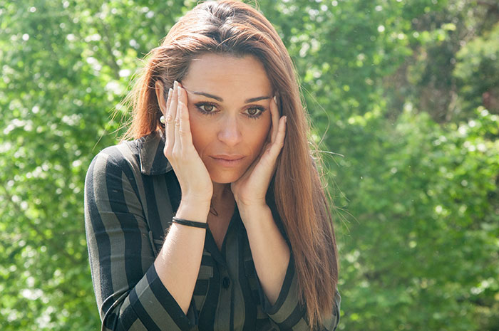 Worried woman outdoors holding her head, representing stress about child&rsquo;s severe allergy and MIL ignoring health risks.