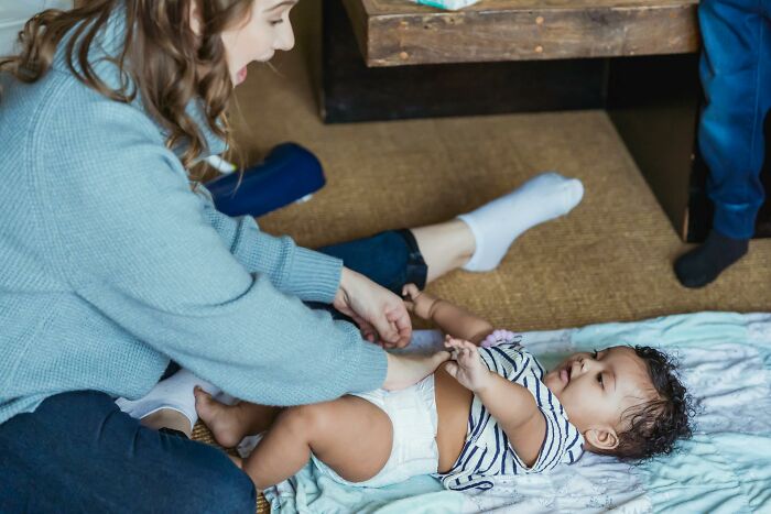 Mom watches as dad takes care of son for the first time while changing his diaper and playing on the floor.