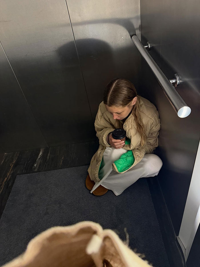 Bella Hadid sitting in a hospital elevator corner with a cast on her arm, holding a coffee cup, showing invisible suffering.
