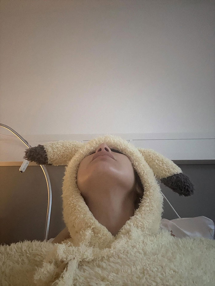 Person wearing a fluffy hooded garment with ears, lying back in a hospital setting after years of invisible suffering.