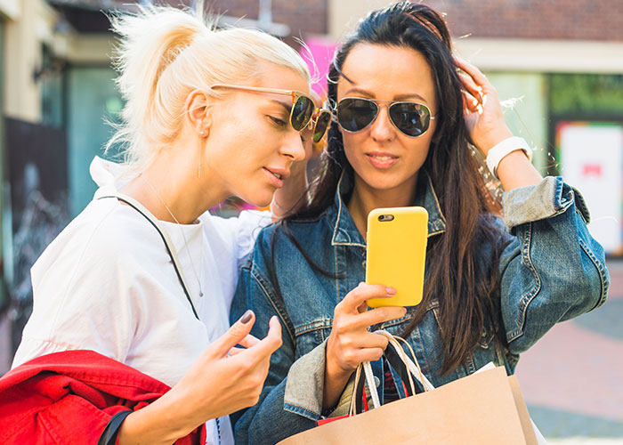 Two women outdoors, one showing something on her phone while the other listens, highlighting issues of privacy and trust.