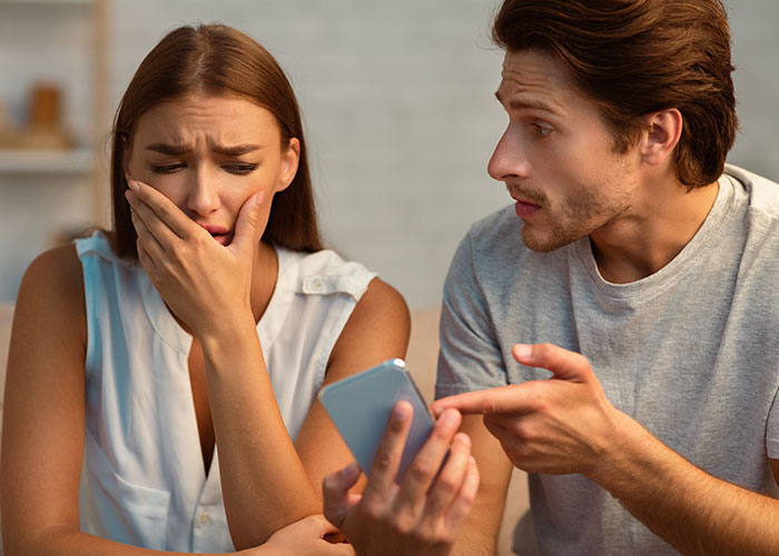 Woman upset and covering her mouth while a man holds a phone, illustrating privacy violation and cutting off a long-term friend.