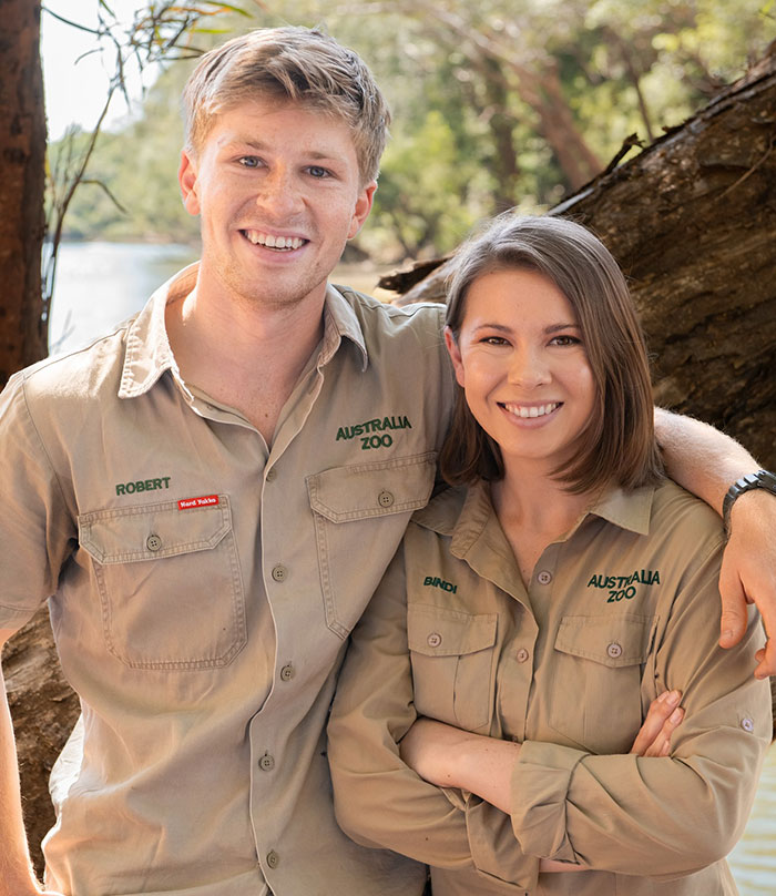Bindi Irwin and Robert in Australia Zoo uniforms smiling outdoors, highlighting Bindi Irwin's move from Australia. Bindi Irwin and Robert in Australia Zoo uniforms smiling outdoors, highlighting Bindi Irwin's move from Australia.
